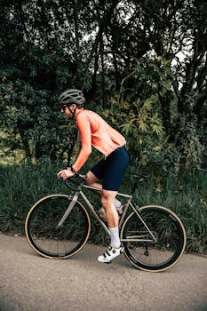 A man riding a bicycle on a road surrounded by lush greenery, wearing a helmet and sports attire.