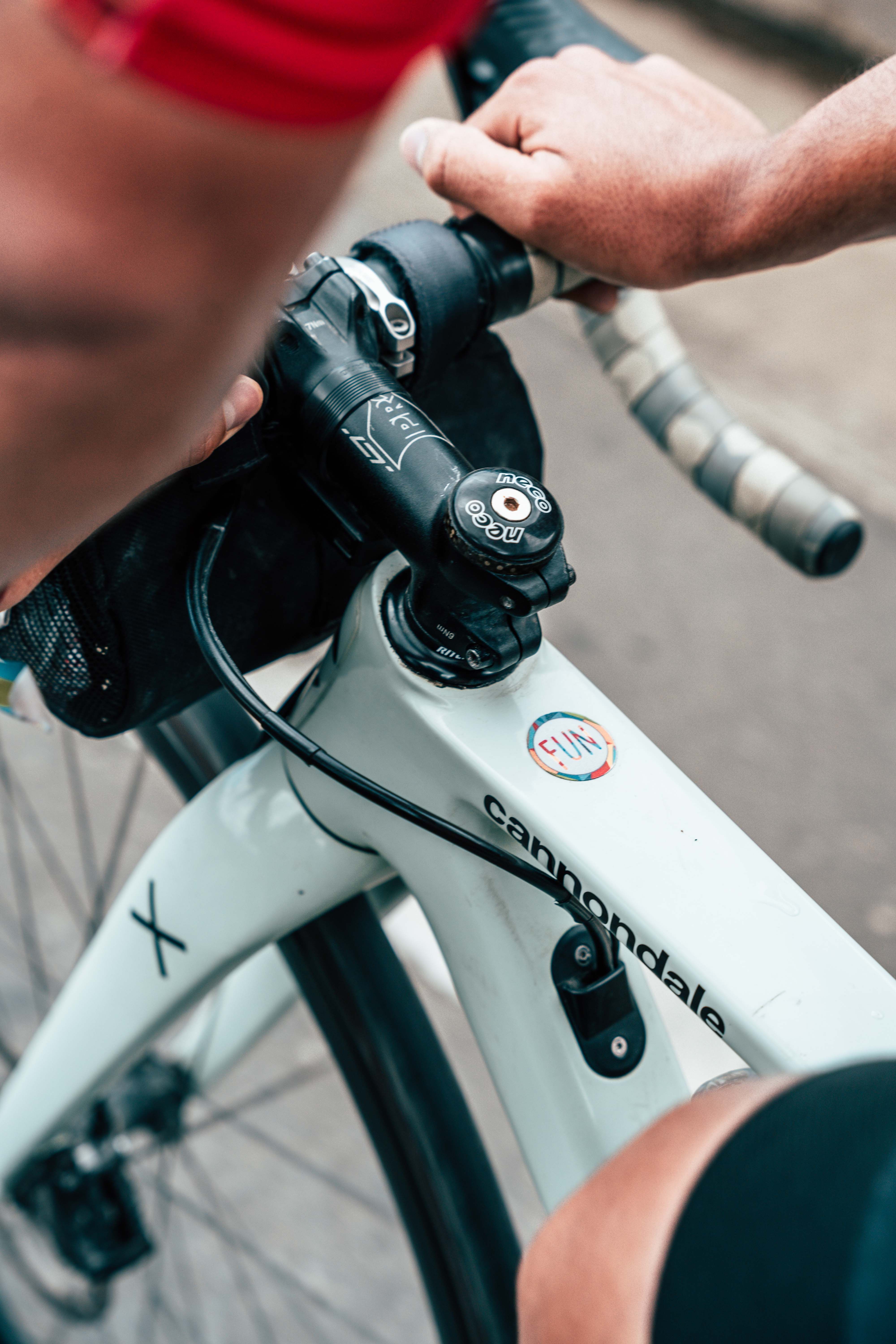 Detailed view of a cyclist's hands gripping a white Cannondale bike's handlebars, emphasizing sport and biking activity.