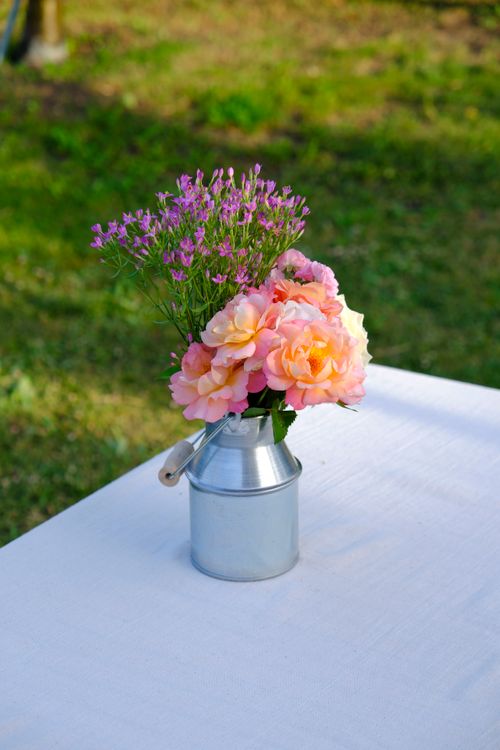 Free Colorful bouquet arrangement in a rustic metal vase on an outdoor table, perfect for garden parties. Stock Photo