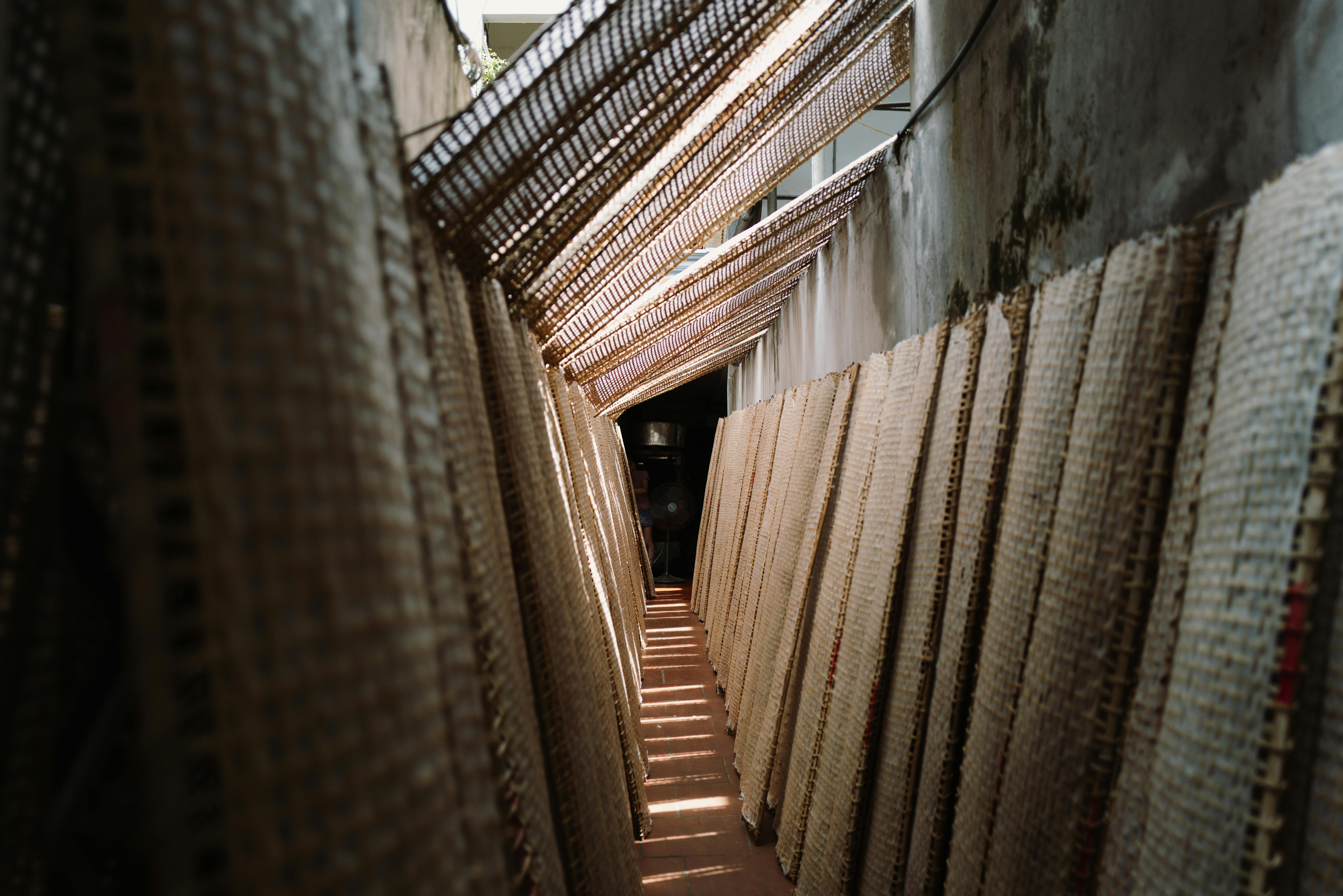 Narrow alley in Bắc Giang, Vietnam, lined with drying rice paper racks under sunlight.