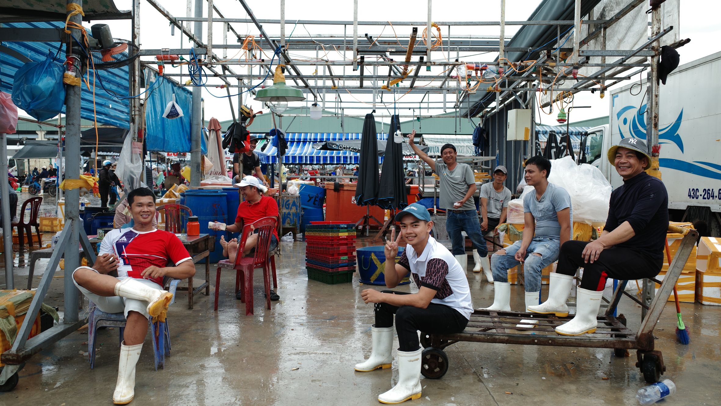 Group of men working and relaxing at a fish market in Đà Nẵng, Vietnam, amid vibrant market activity.