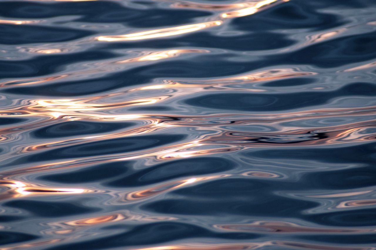 close up of shimmering water ripples reflecting sunlight at sunset cre