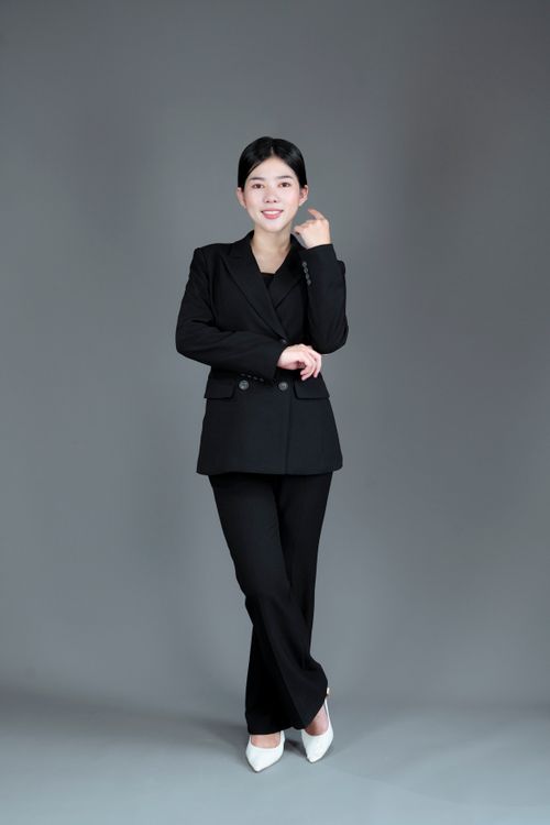 Free Portrait of an Asian businesswoman confidently posing in a studio wearing a black suit against a grey background. Stock Photo