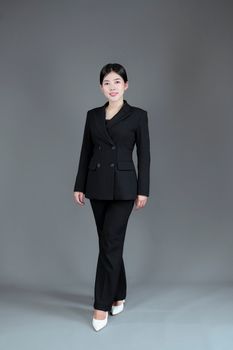Asian businesswoman in a black suit poses confidently in a studio setting.