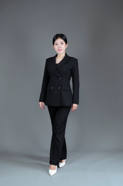 Asian businesswoman in a black suit poses confidently in a studio setting.