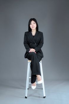 Asian businesswoman in a suit posing confidently on a stool in a professional studio setting.