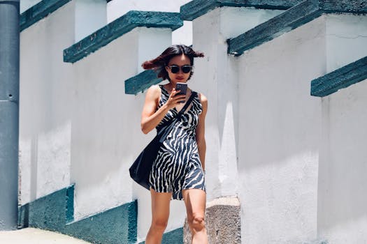Woman in zebra dress walking outdoors using smartphone, urban lifestyle.
