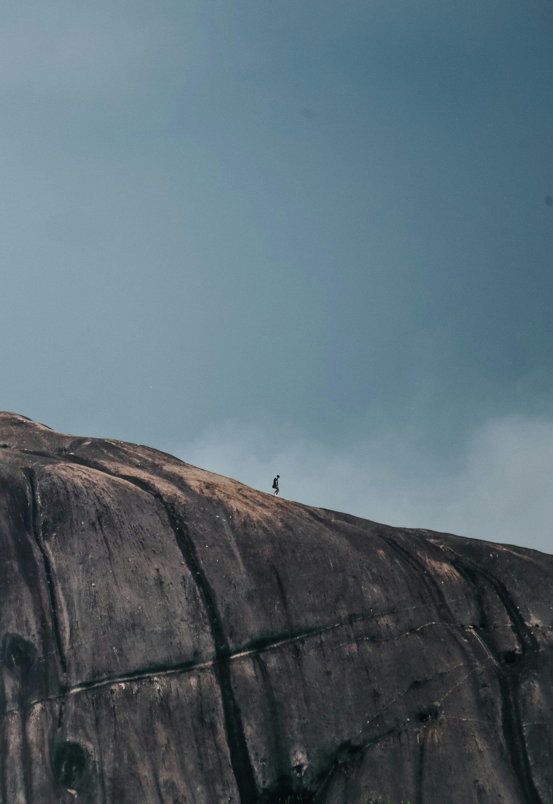 Lone hiker traversing a vast rocky mountain slope under an overcast sky.