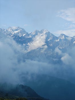 A scenic view of snow-capped mountains enveloped in mist and clouds, evoking tranquility.