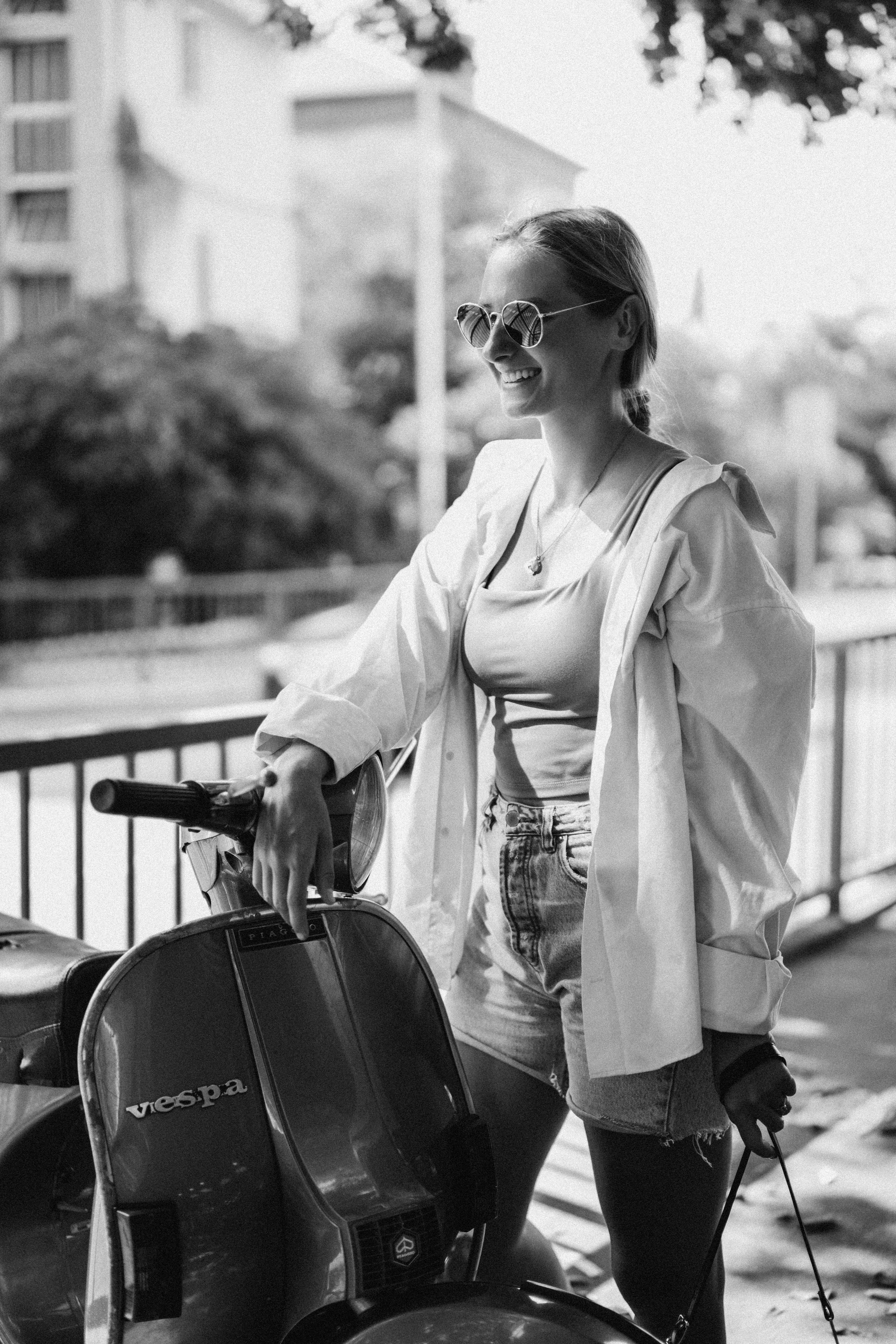 Smiling woman in sunglasses poses with Vespa scooter in Split, Croatia.