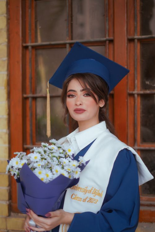 Free Middle Eastern woman in academic dress holding bouquet, Baghdad graduation moment. Stock Photo