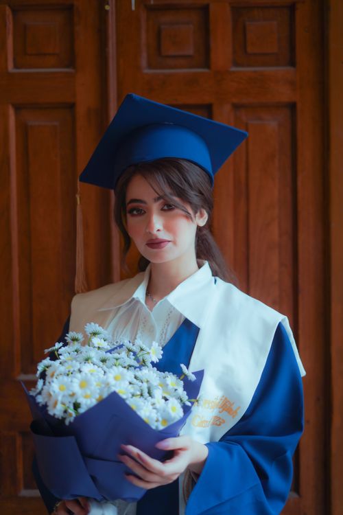 Free Graduation photo of an elegant woman in a blue gown and cap, holding a floral bouquet. Stock Photo