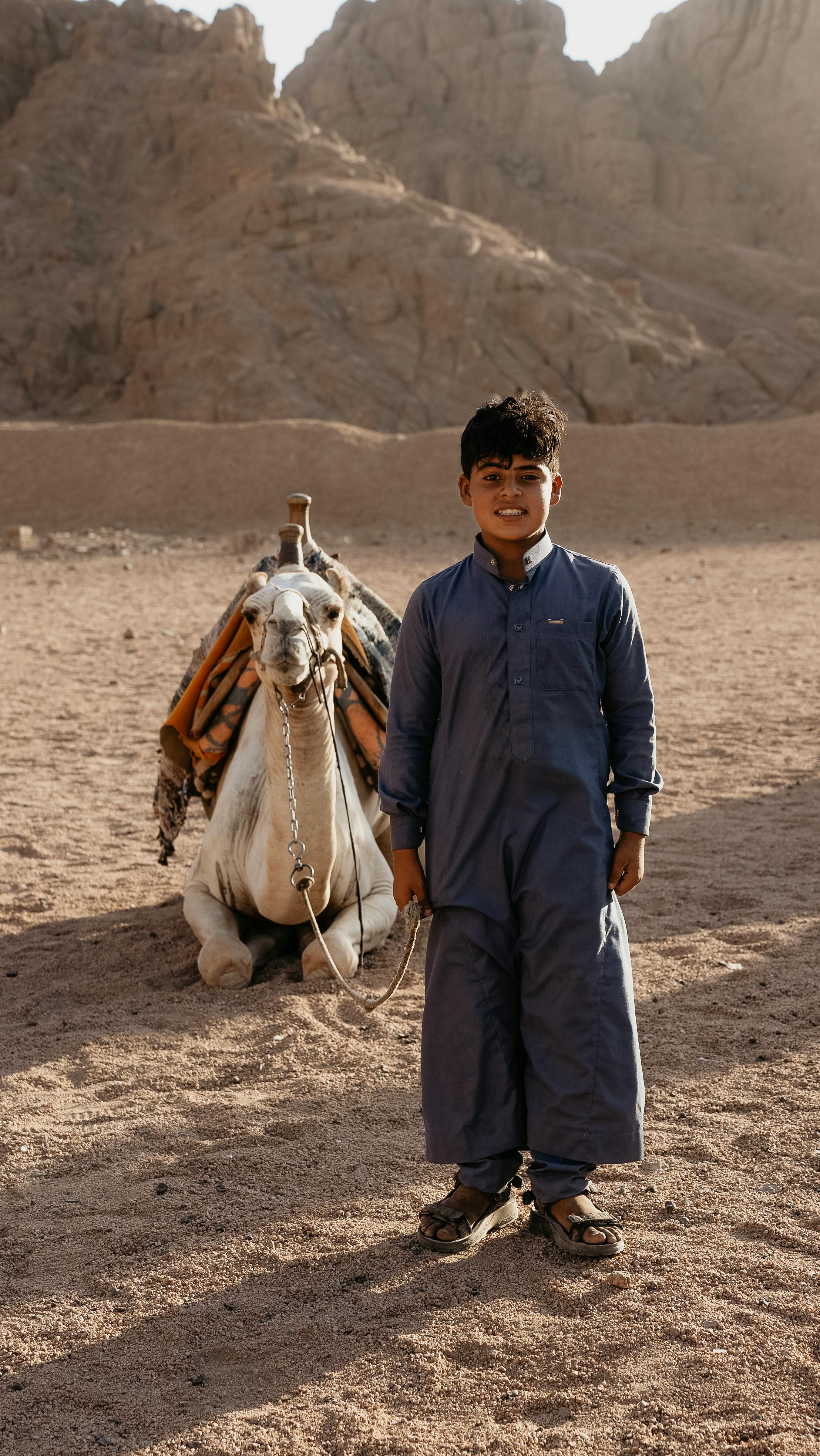 Boy in traditional clothing with camel in the arid desert of Sharm El-Sheikh, Egypt.