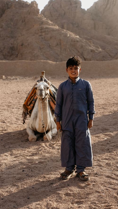 Free Boy in traditional clothing with camel in the arid desert of Sharm El-Sheikh, Egypt. Stock Photo