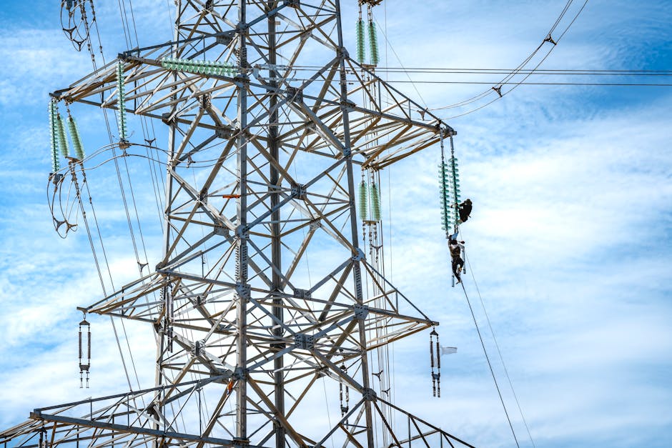 Workers performing maintenance on a high voltage power line against a blue sky.