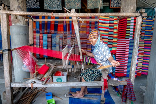 A woman is weaving a colorful cloth on a loom