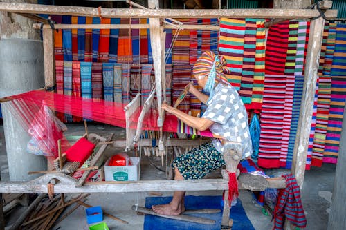 A woman is weaving a colorful cloth on a loom