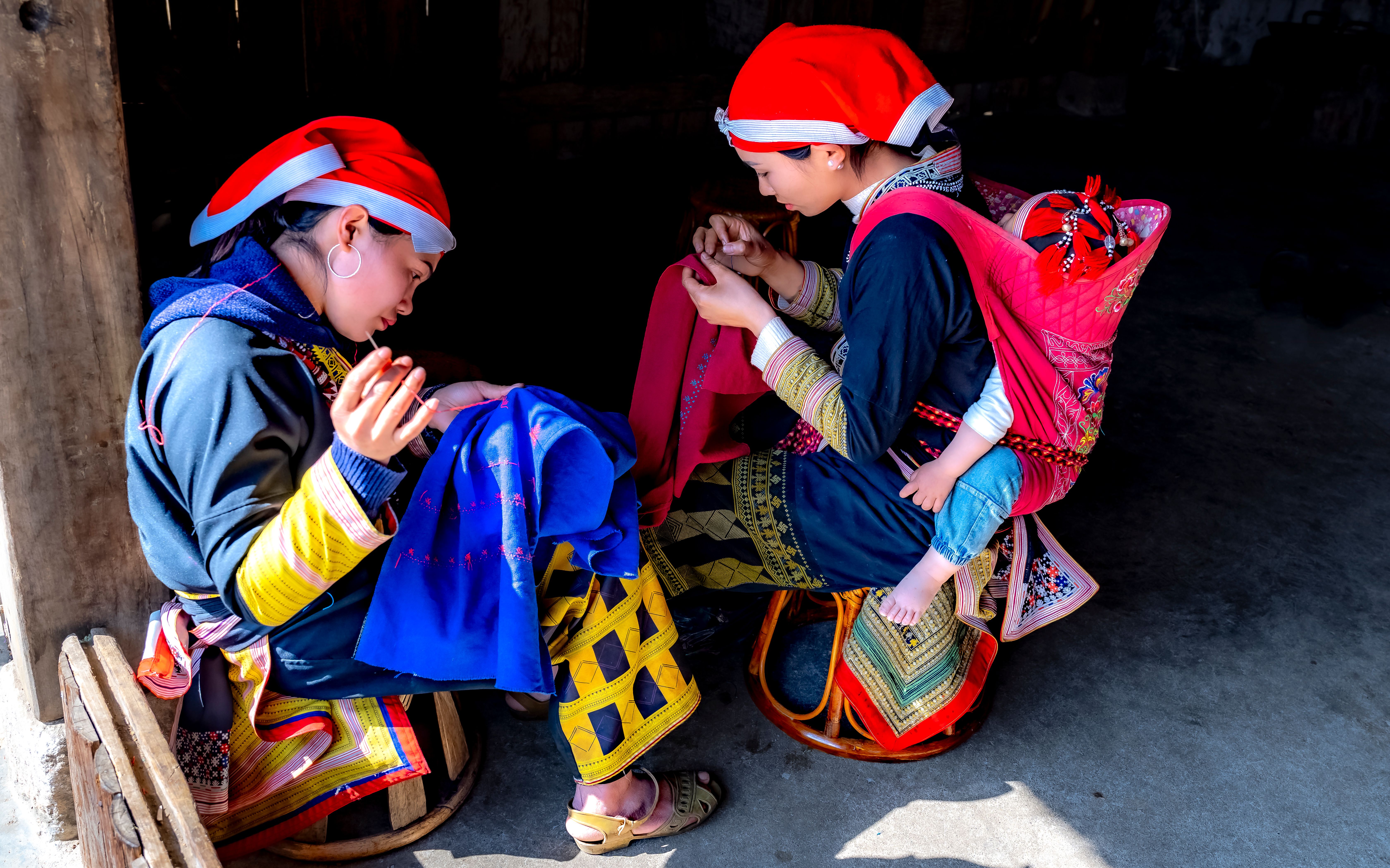 Two women in traditional clothing sewing indoors