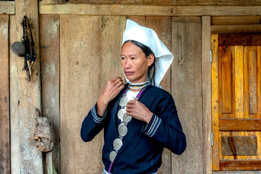 Portrait of a woman in traditional clothing, standing in a rustic setting.