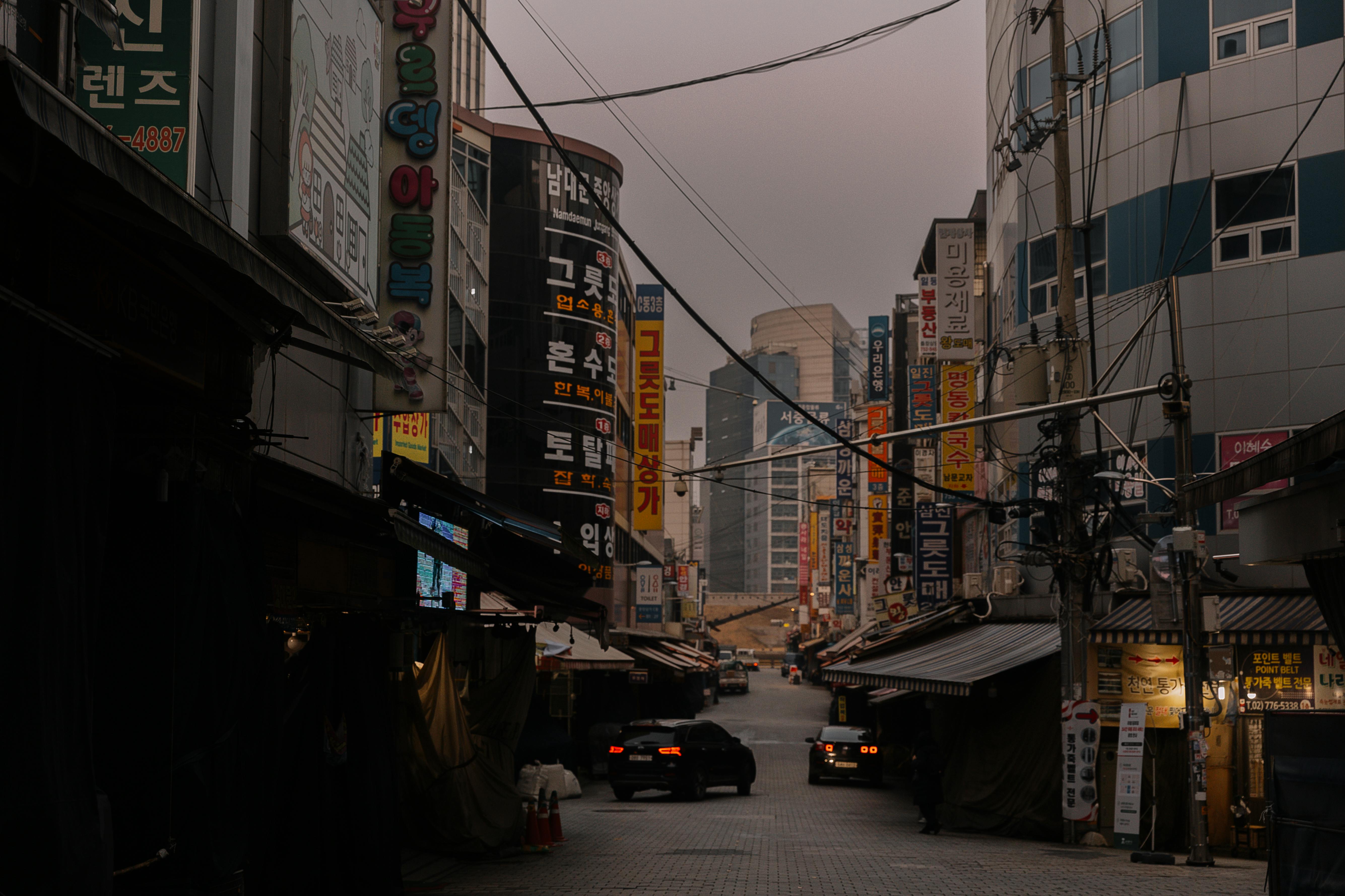 A bustling urban street lined with neon signs and buildings under a moody dusky sky, creating a vibrant city atmosphere.