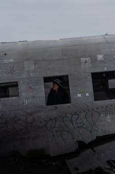 Woman in a hat looking out from an abandoned airplane wreckage.