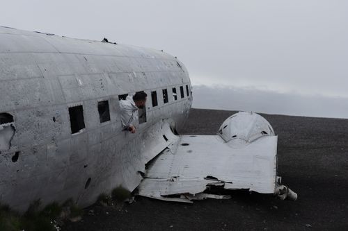 Free A man leans out of an abandoned plane wreck in a desolate outdoor setting, creating a dramatic scene. Stock Photo