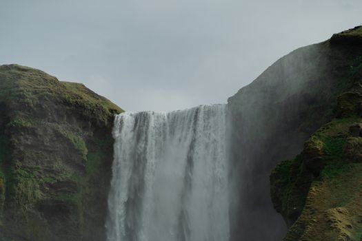 Breathtaking view of Skogafoss waterfall cascading between lush green cliffs in Iceland.