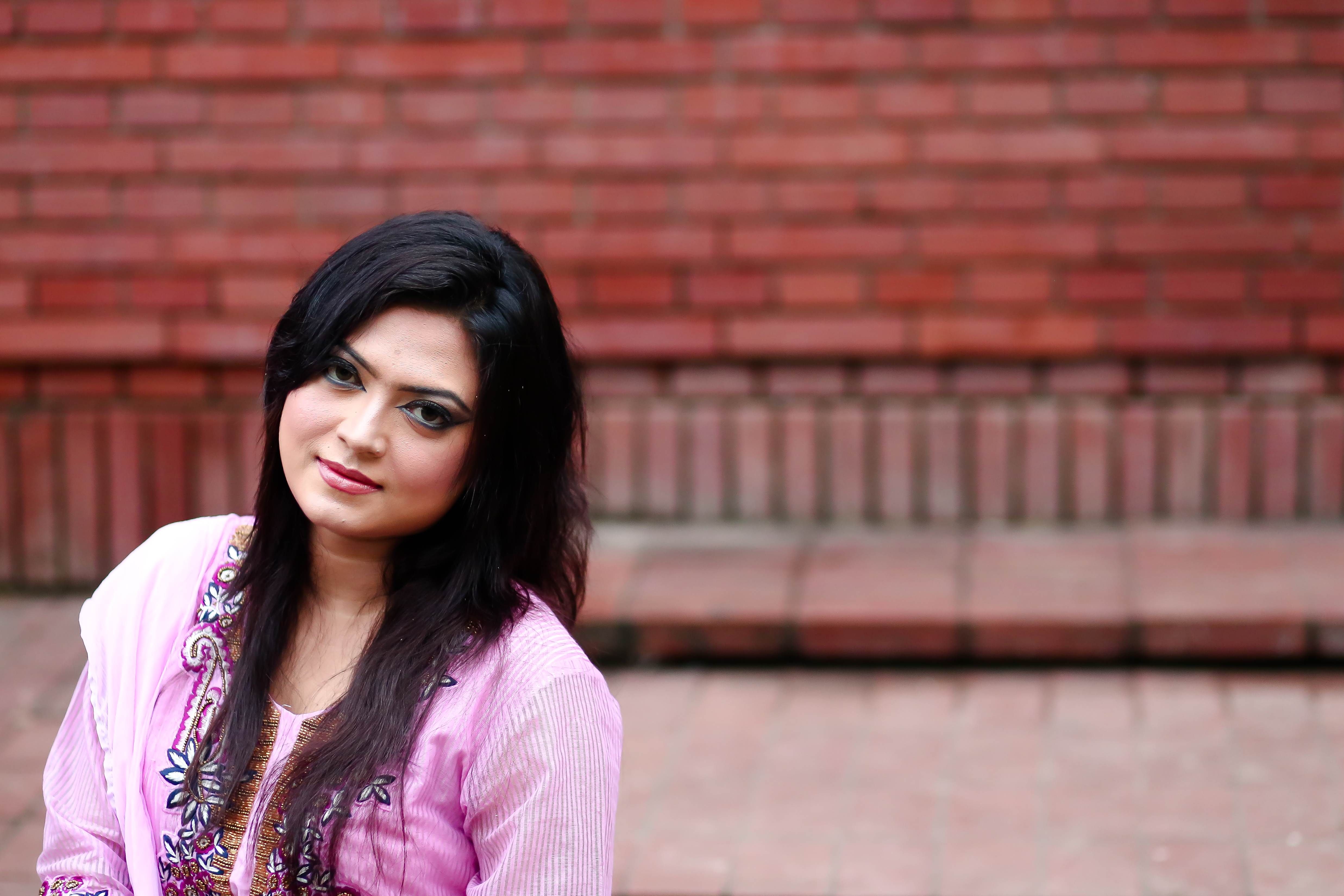 Elegant portrait of a woman in traditional pink clothing against a brick wall.