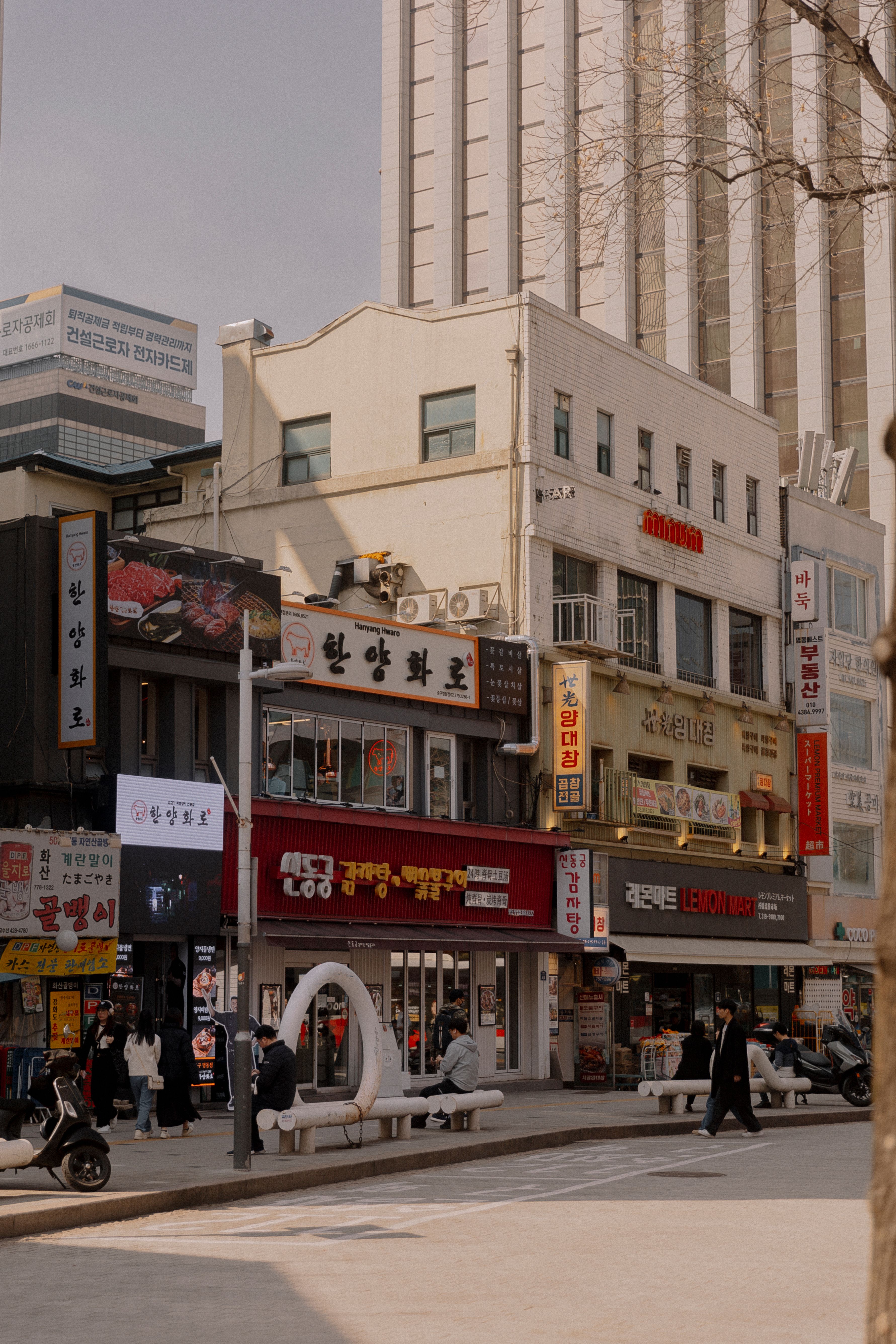 Lively city street in Seoul with shops, signs, and pedestrians during the day.