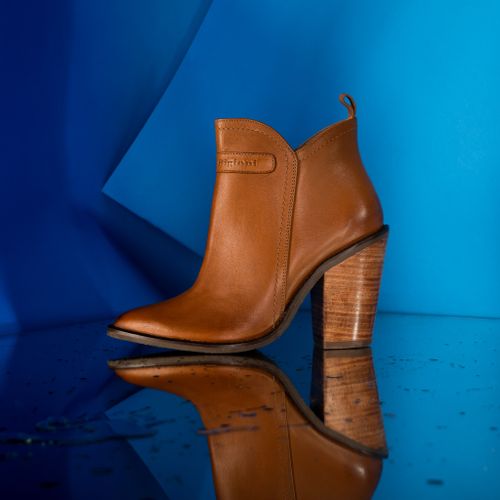 Free Elegant brown leather boot with high heels showcased on a blue background and reflective surface. Stock Photo