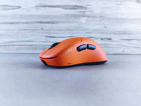 Sleek orange Lamzu wireless mouse displayed on a wooden texture background, perfect for tech enthusiasts.