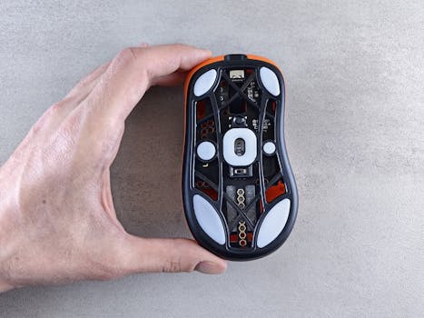 Detailed view of the bottom of an optical computer mouse being held by a hand on a textured surface.