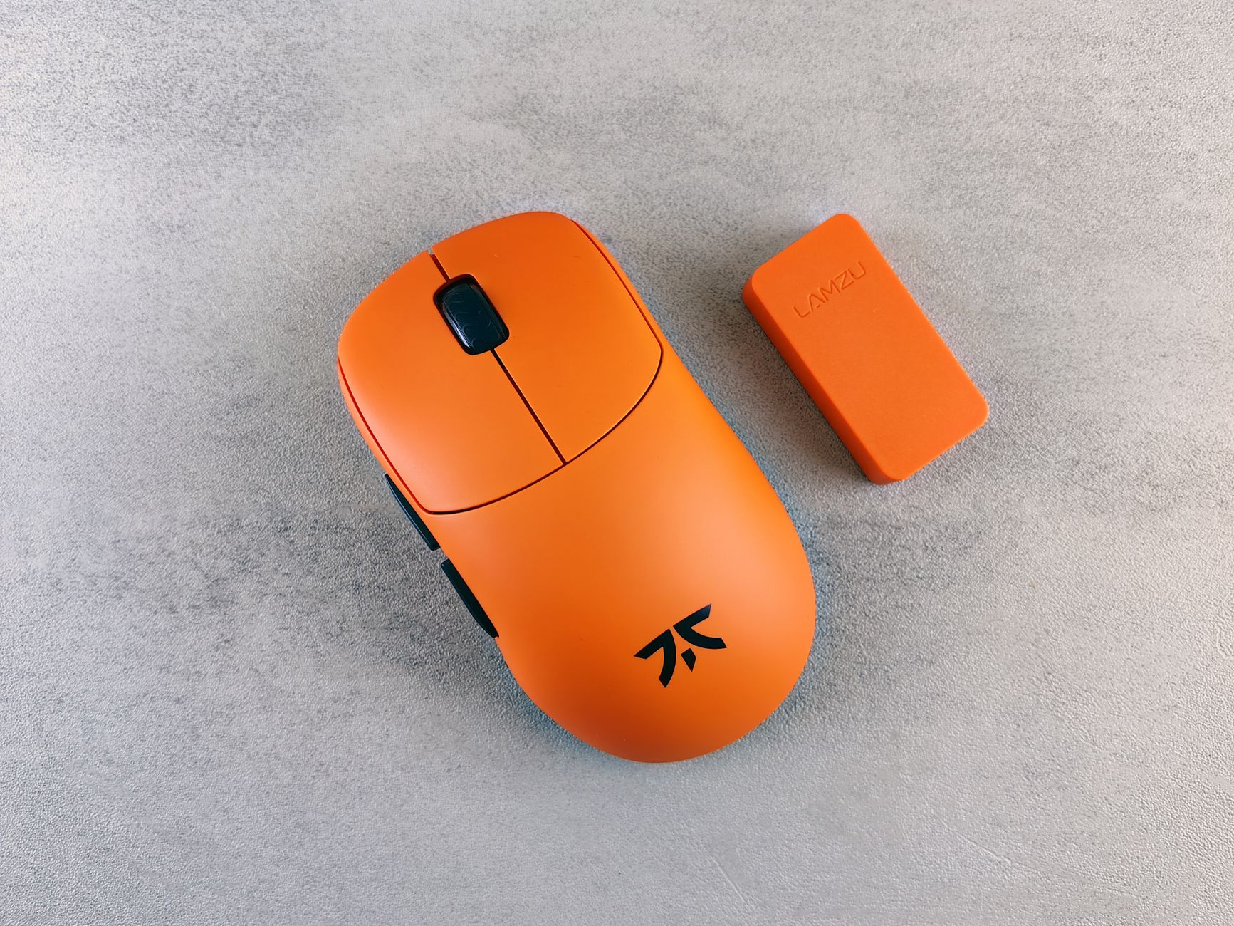 Close-up of a bright orange gaming mouse with a matching component on a textured surface.