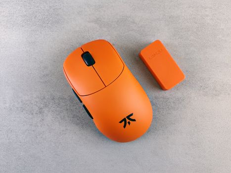 Close-up of a bright orange gaming mouse with a matching component on a textured surface.