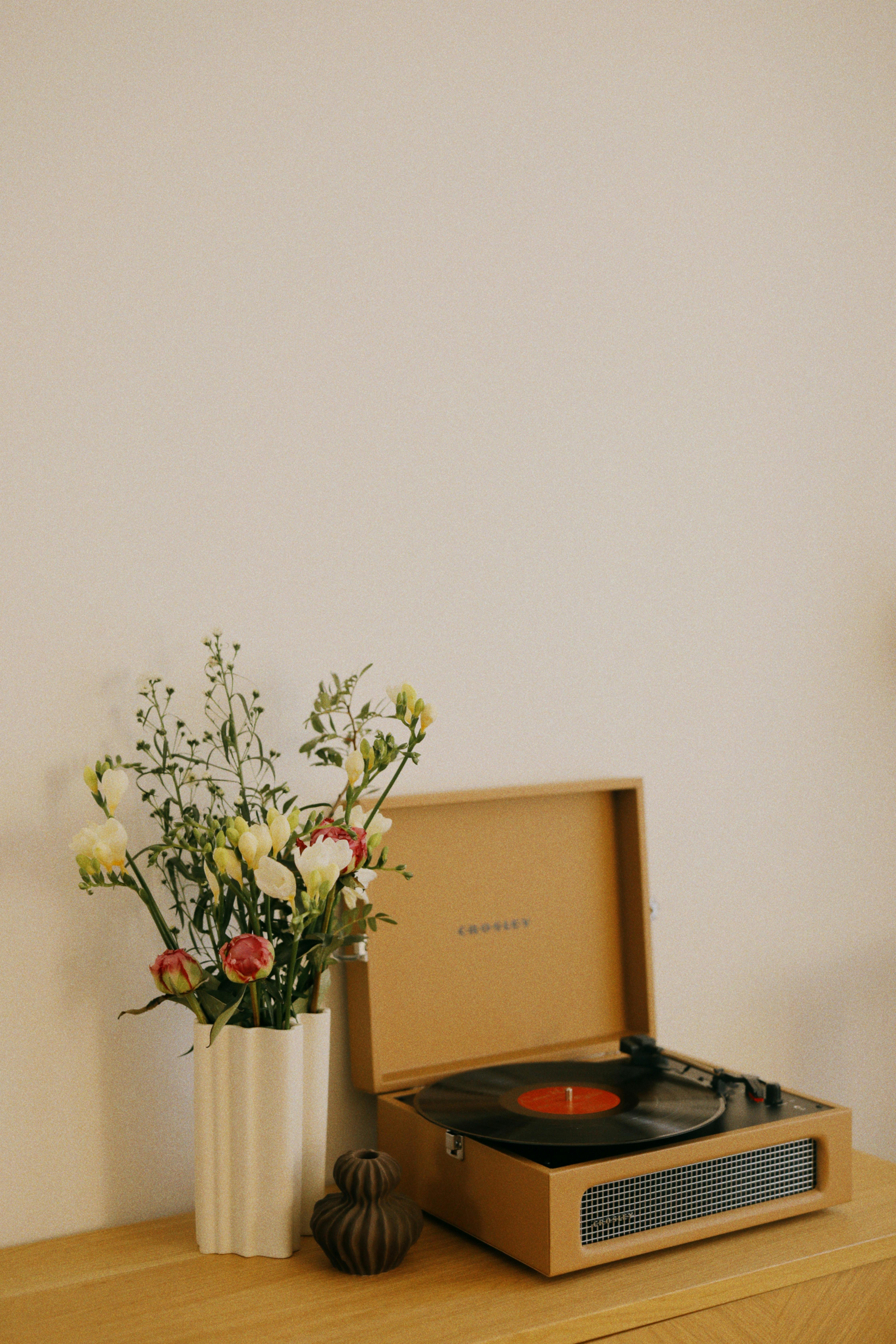 A minimalist setup featuring a vintage record player and vase of flowers on a wooden dresser, ideal for modern living spaces.