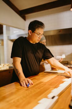 Asian man in black t-shirt working at a kitchen counter, focused on meal preparation.