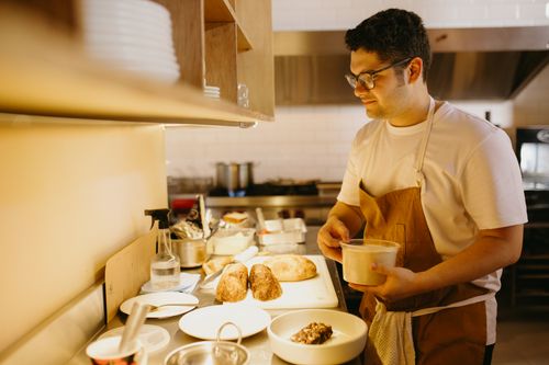 Free Adult male chef preparing food in a commercial kitchen with bread and ingredients. Stock Photo