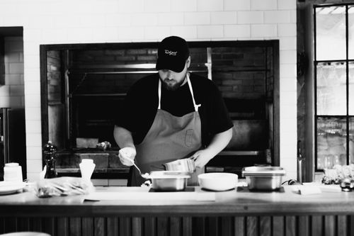 Free A chef wearing an apron prepares a meal in a rustic kitchen. Black and white photography. Stock Photo