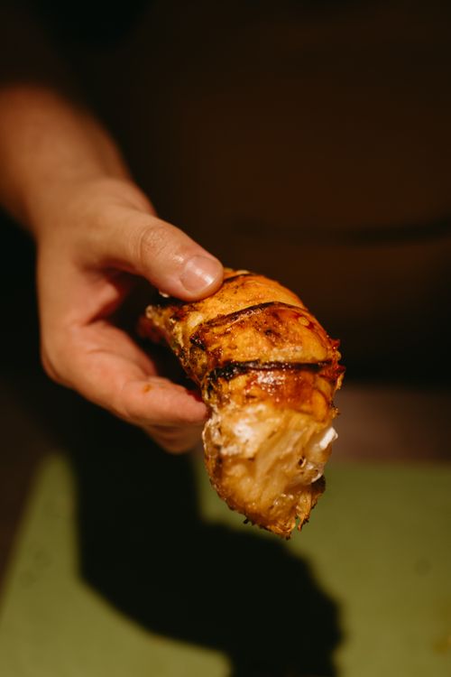 Free Close-up of a hand holding a grilled chicken piece, highlighting its texture and color. Stock Photo