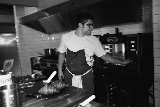 Chef in apron working in a modern kitchen, using an oven to prepare food.