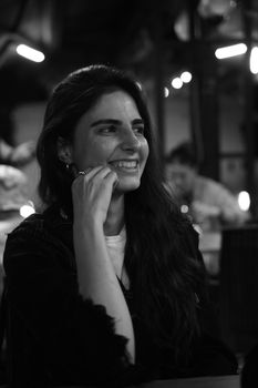 A candid black and white portrait of a smiling woman enjoying a relaxed moment indoors.