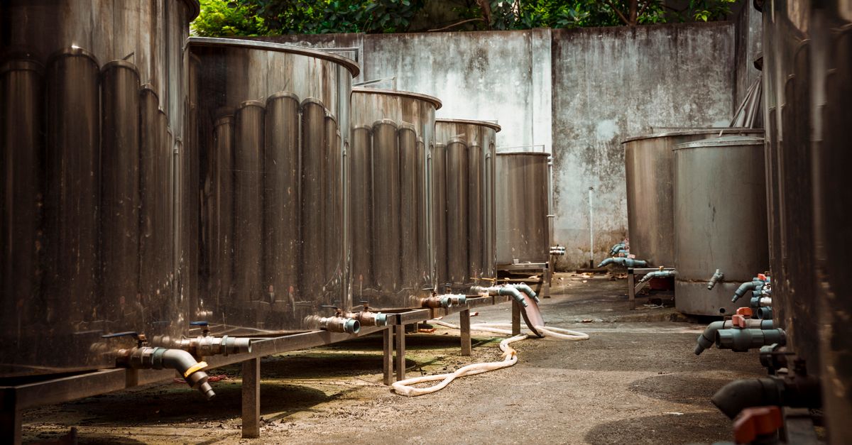 Outdoor view of large industrial metal tanks with connected pipes and concrete surroundings.