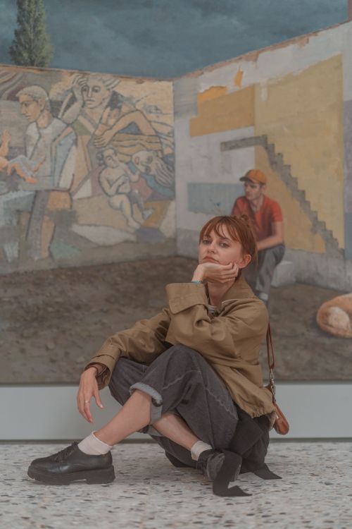 Free Woman in a trench coat poses thoughtfully against a vibrant mural in Venice, Italy. Stock Photo