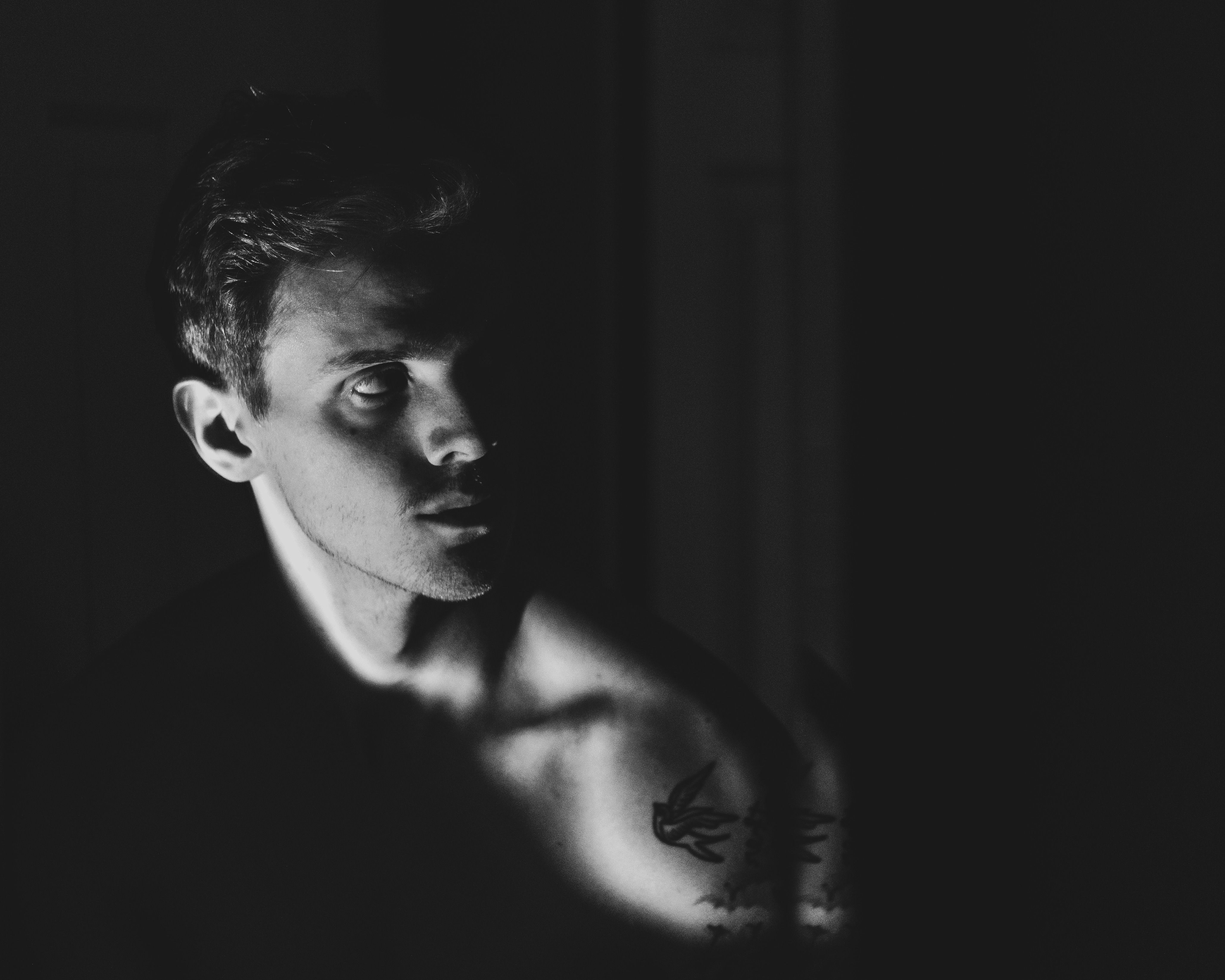 Dramatic black and white portrait capturing a tattooed man in striking chiaroscuro lighting.. dramatic, black, white