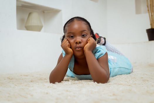 A young girl in a blue dress lying on a soft white carpet, indoors.
