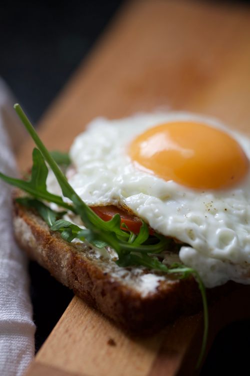 Free Close-up of a savory avocado toast topped with a perfectly fried egg, arugula, and ripe tomato. Stock Photo