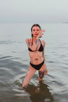Tattooed woman standing in the sea in a bikini, displaying unique body art.