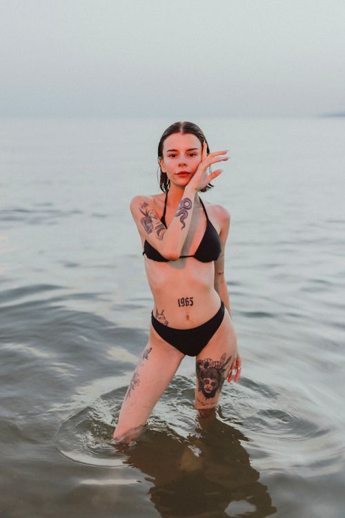 Free Tattooed woman standing in the sea in a bikini, displaying unique body art. Stock Photo