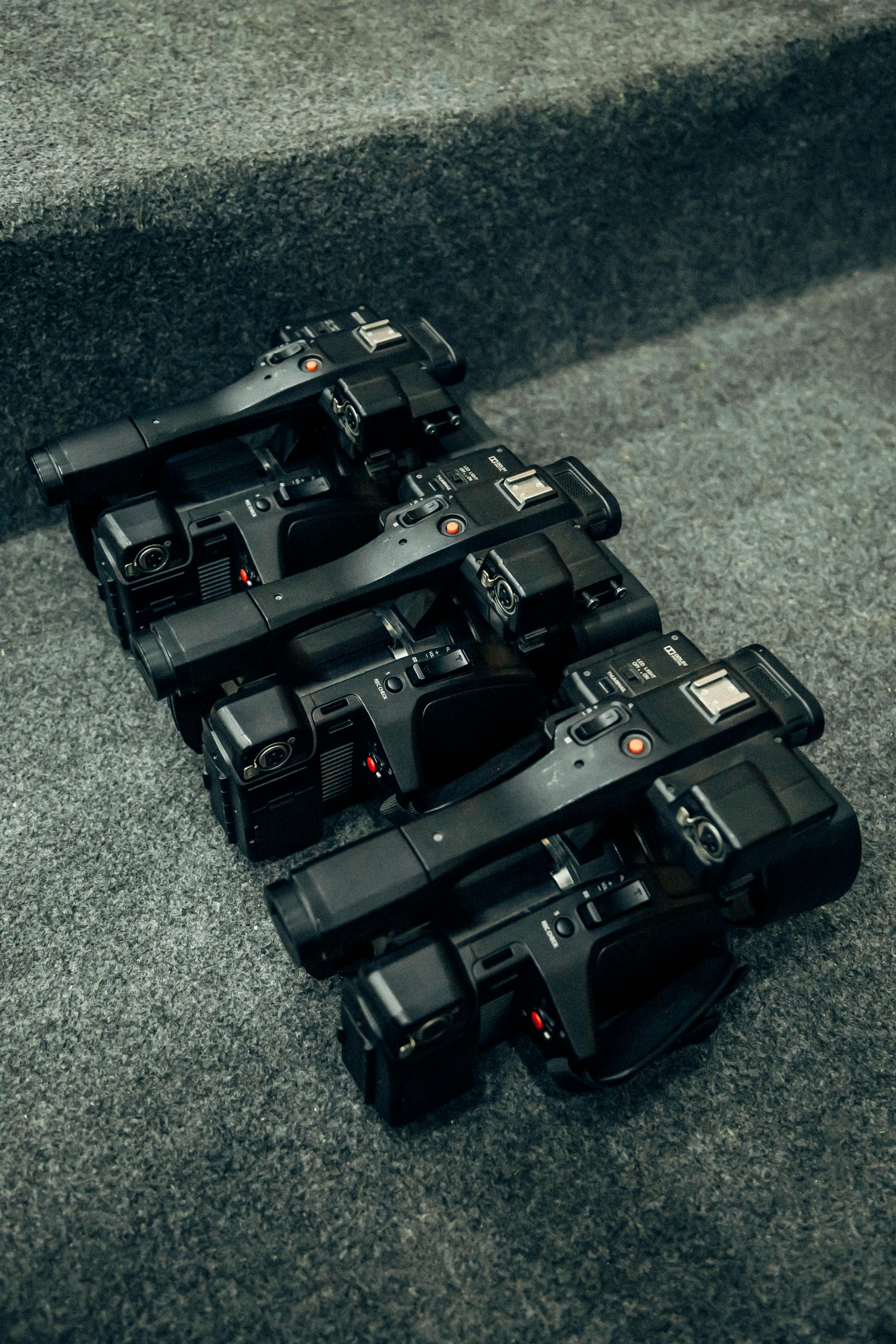 Four professional video camcorders neatly arranged on a carpeted surface, showcasing equipment organization.