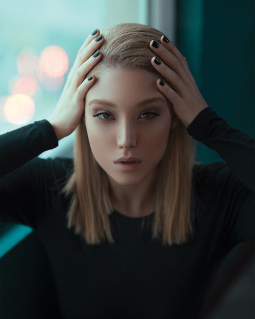 Close-up portrait of a young woman with blond hair posing indoors with a serious expression.
